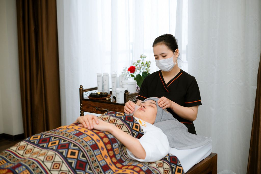 A massage therapist performs a soothing facial treatment on a client in a cozy spa room.