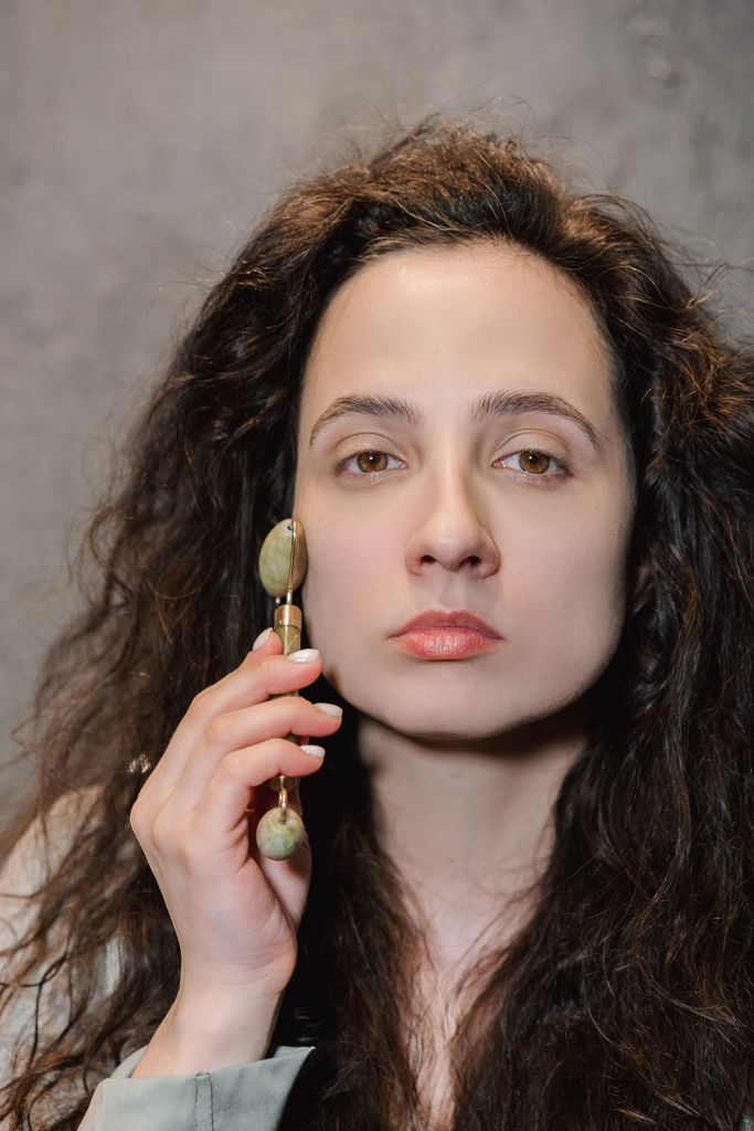 Close-up of a woman using a jade roller for skincare routine, promoting facial care.